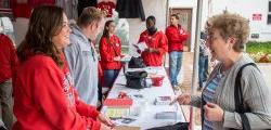 Girl wearing red Montclair State University sweatshirt helping an elderly woman at Homecoming tent.